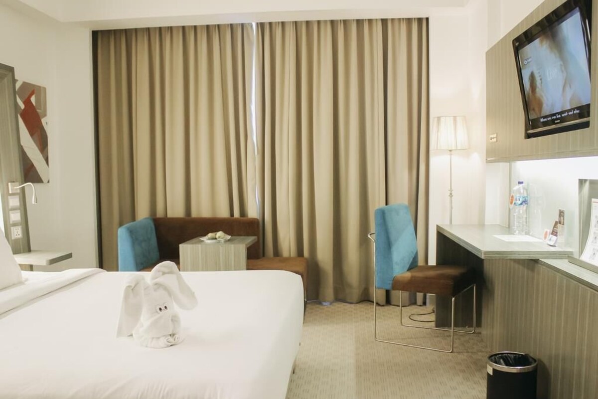 A hotel room with a bed, two chairs, a desk, a television, and a curtain.