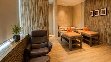 A spa room with a massage table, a massage chair, and a small table with a plant.