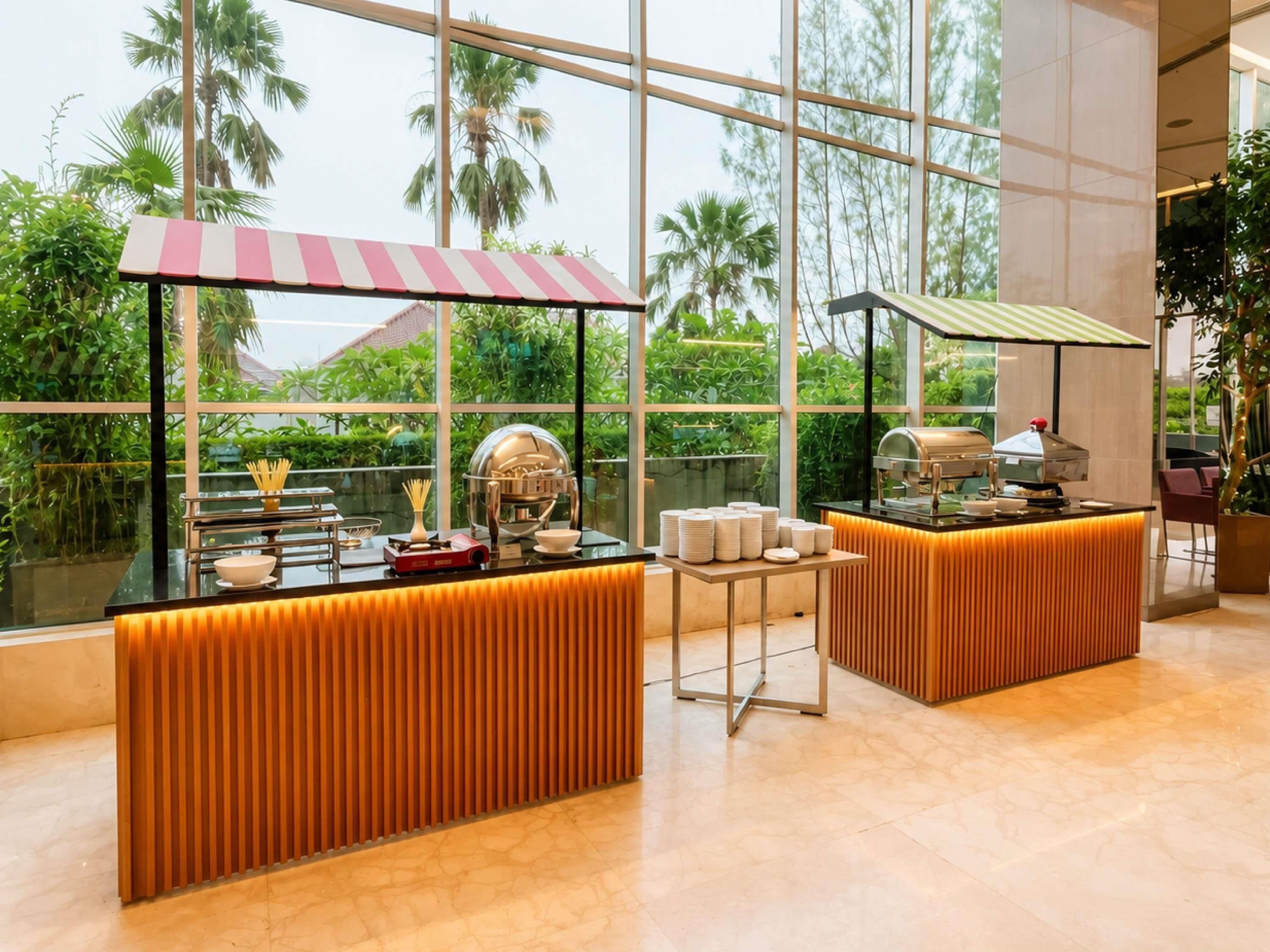 A modern kitchen area with a buffet setup, large windows, and a view of palm trees.