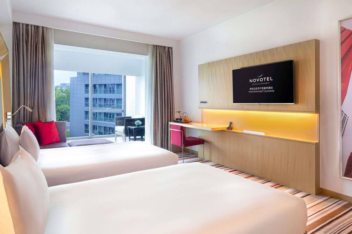 Une chambre d’hôtel avec deux lits, un bureau, une télévision et une vue sur un immeuble.