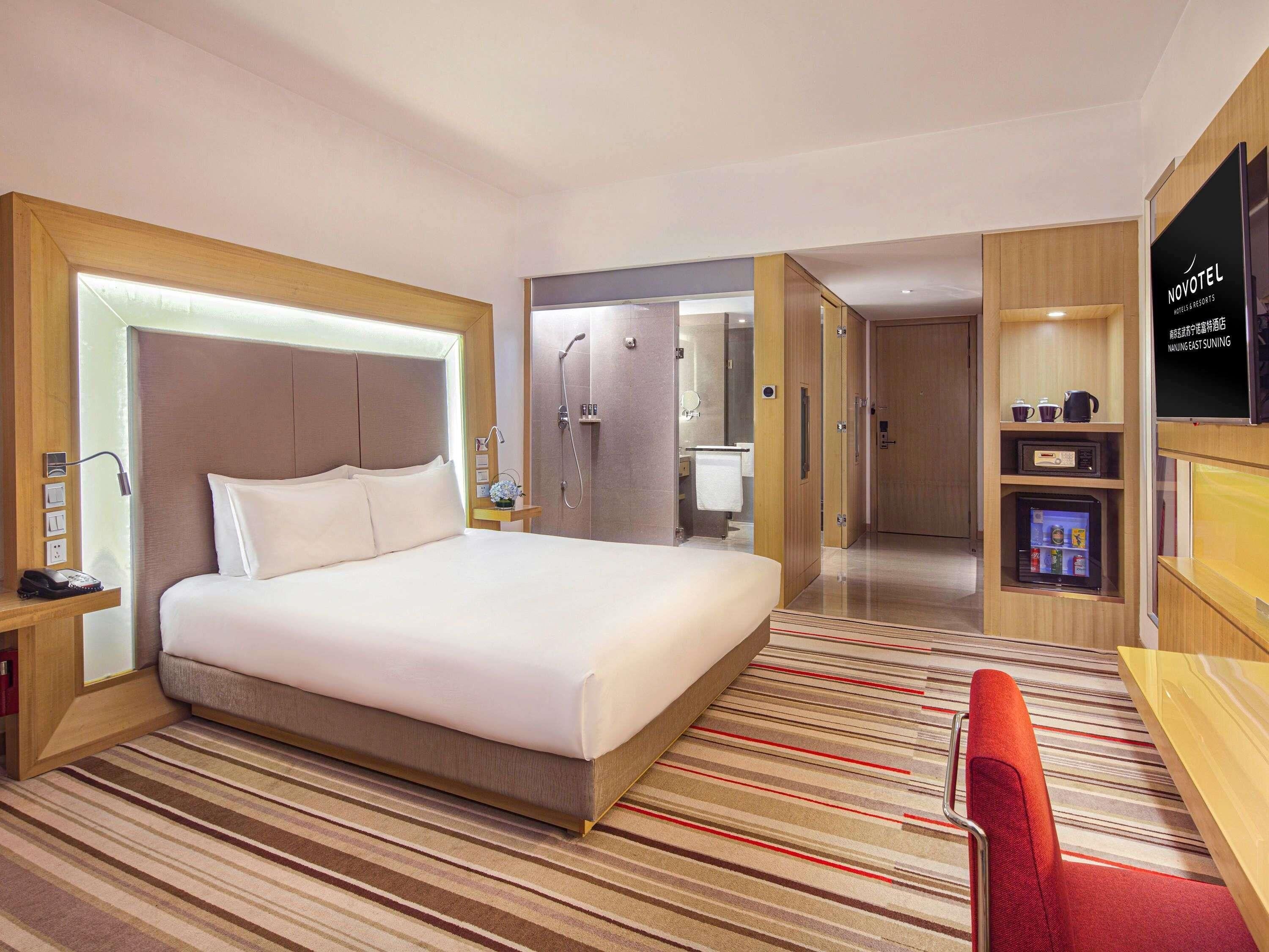 Ein Hotelzimmer mit Bett, Nachttisch, Fernseher, Minibar und einer Duschkabine.
