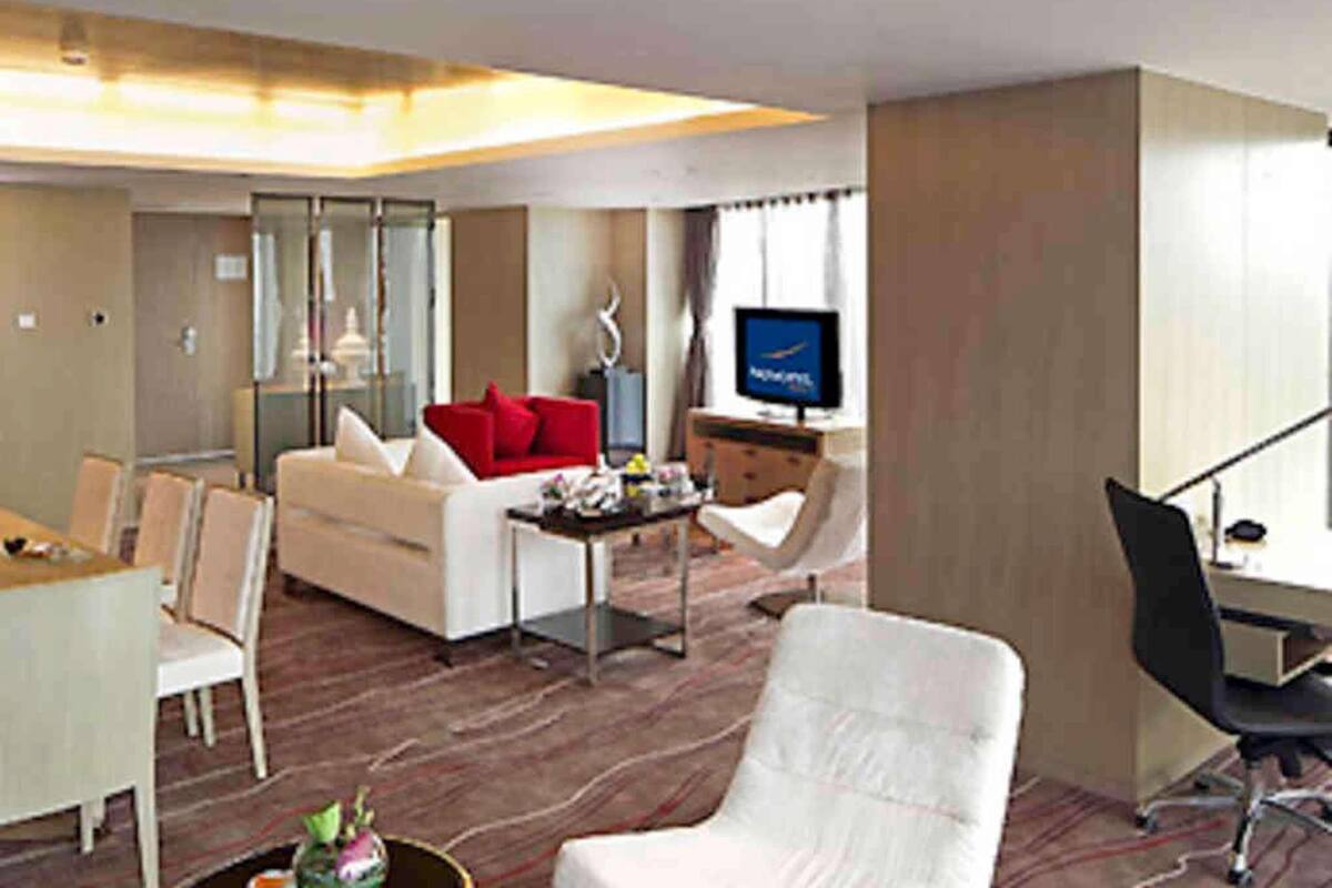 Ein Hotelzimmer mit einem weißen Sofa, einem roten Zierkissen, einem Fernseher, einem Schreibtisch und einem Sessel.