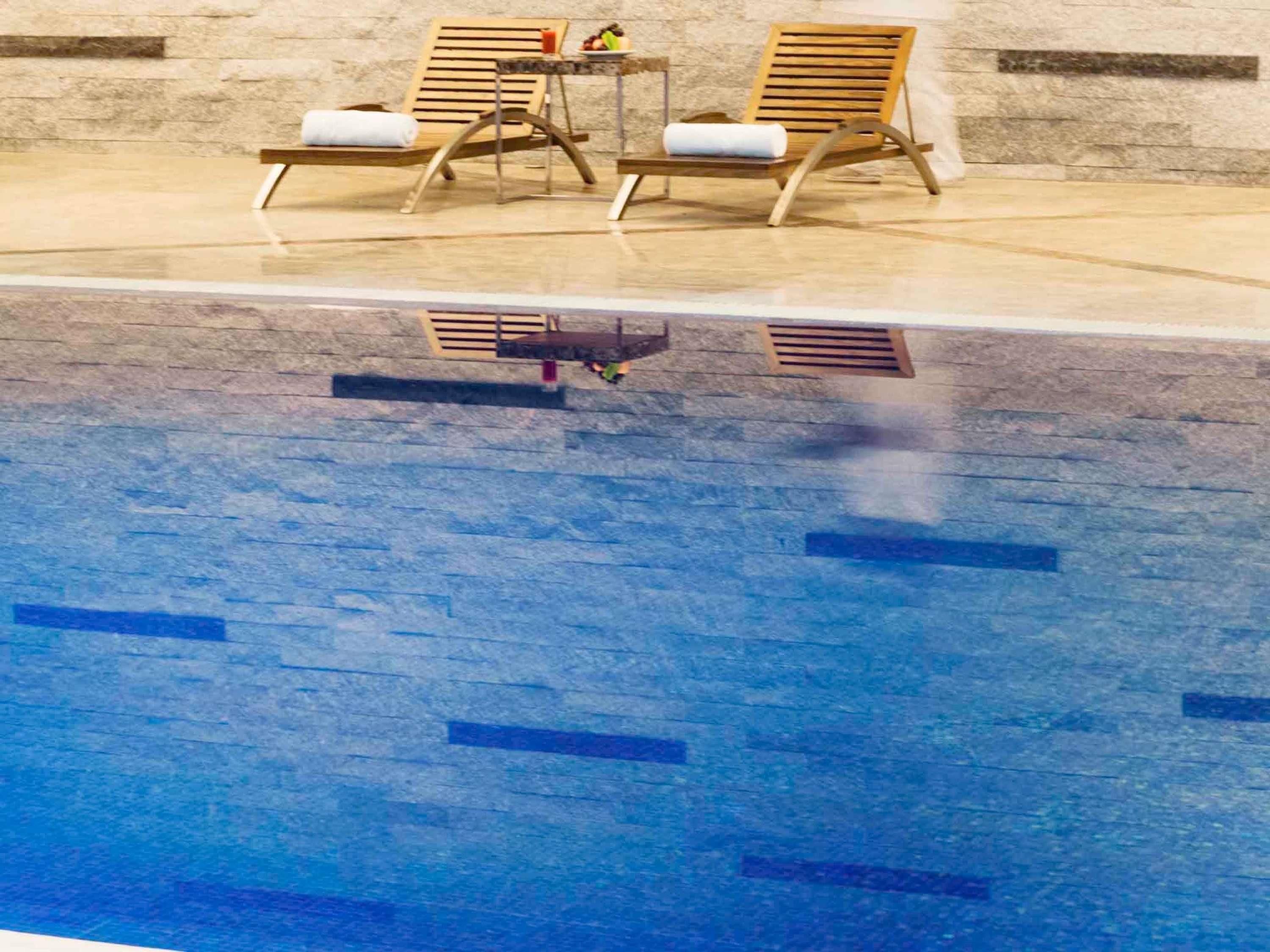 A swimming pool with two wooden lounge chairs and a small table with a fruit bowl.