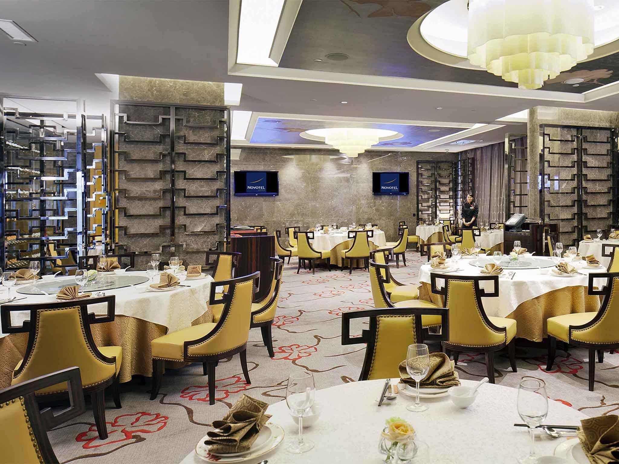 A hotel dining area with round tables, yellow chairs, and a chandelier.