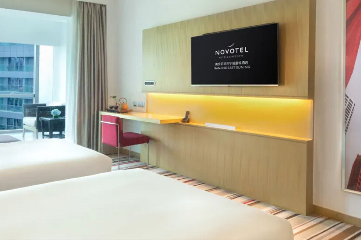 Een hotelkamer met twee bedden, een bureau, een televisie en uitzicht op een gebouw.