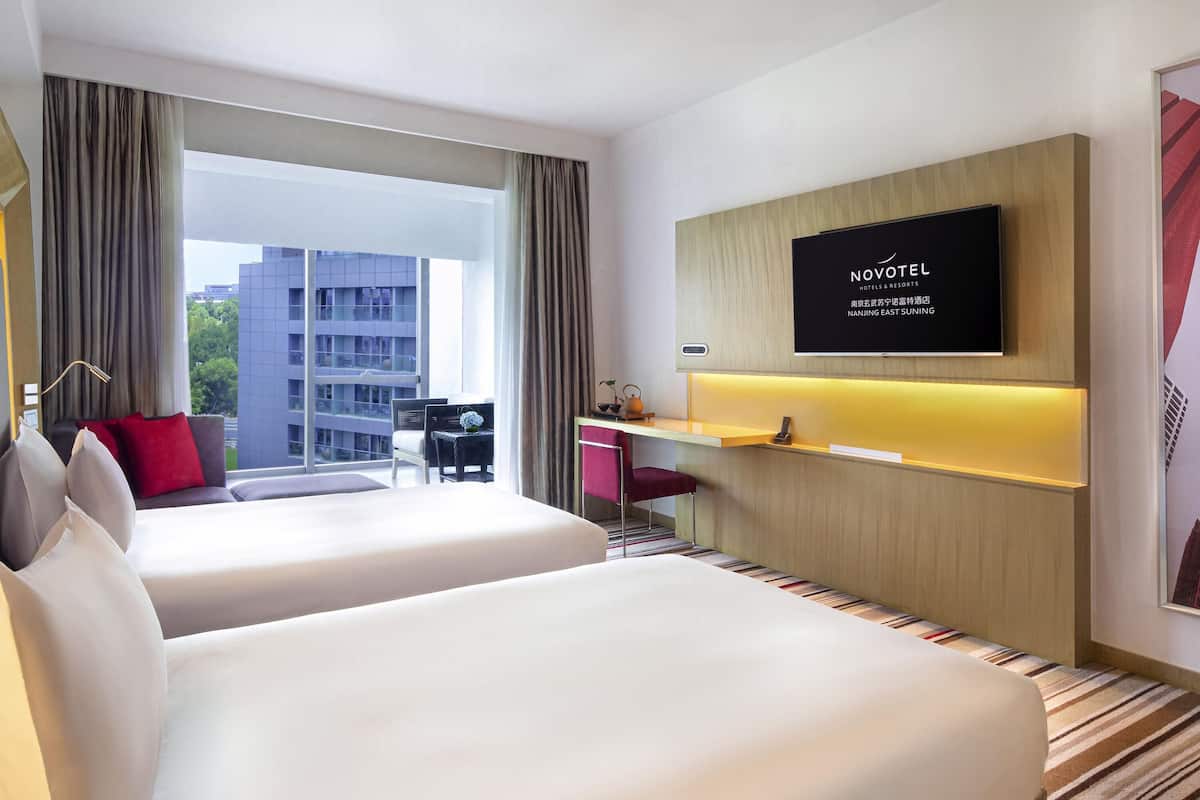 Une chambre d’hôtel avec deux lits, un bureau, une télévision et une vue sur un immeuble.