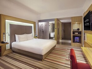 A hotel room with a large bed, a shower, a vanity with a mirror, a TV, and a minibar. - Novotel Nanjing East Suning (Nanjing)