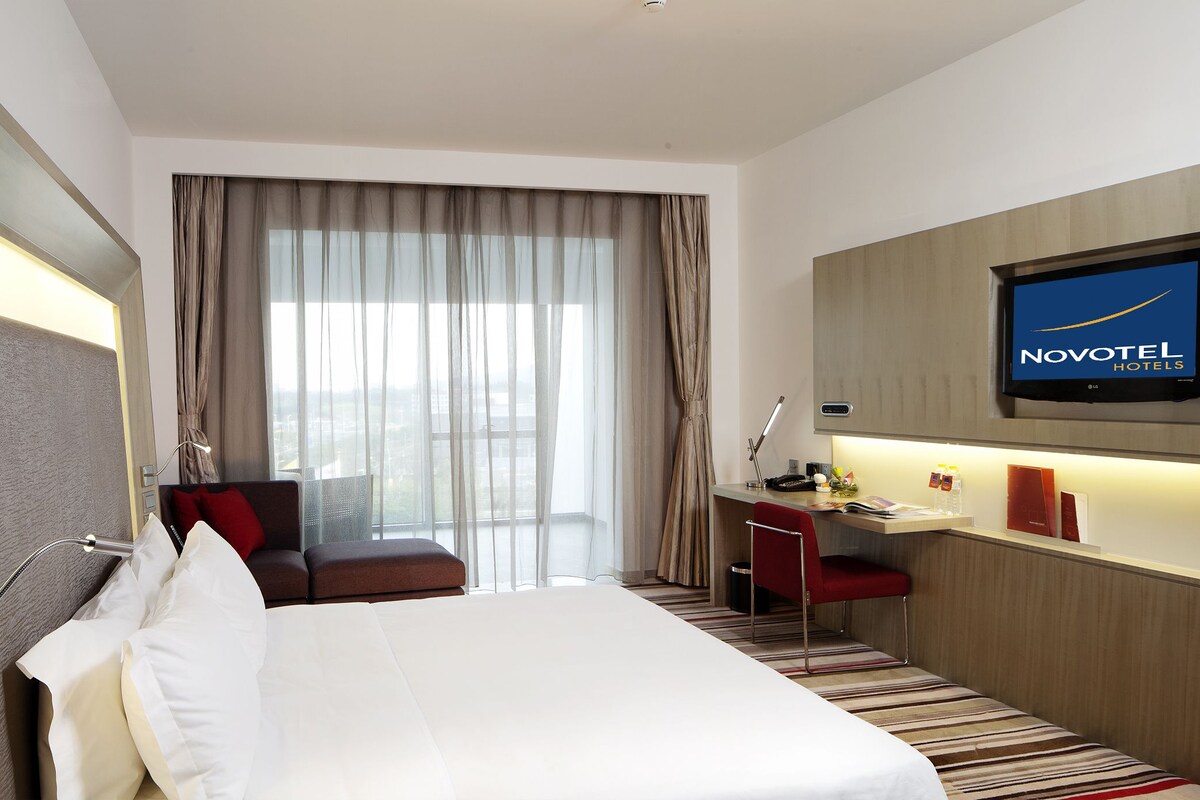 Een hotelkamer met een bed, een bureau, een stoel, een televisie en uitzicht op het omliggende landschap.