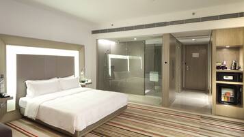 A modern hotel room with a large bed, a TV, a minibar, and a glass-enclosed shower area.