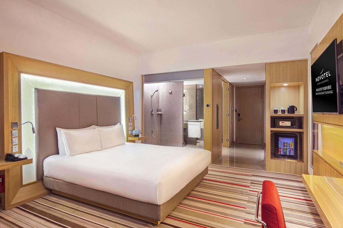 Une chambre d’hôtel équipée d’un lit, d’une table de chevet, d’une commode, d’une télévision, d’un minibar et d’un espace douche.