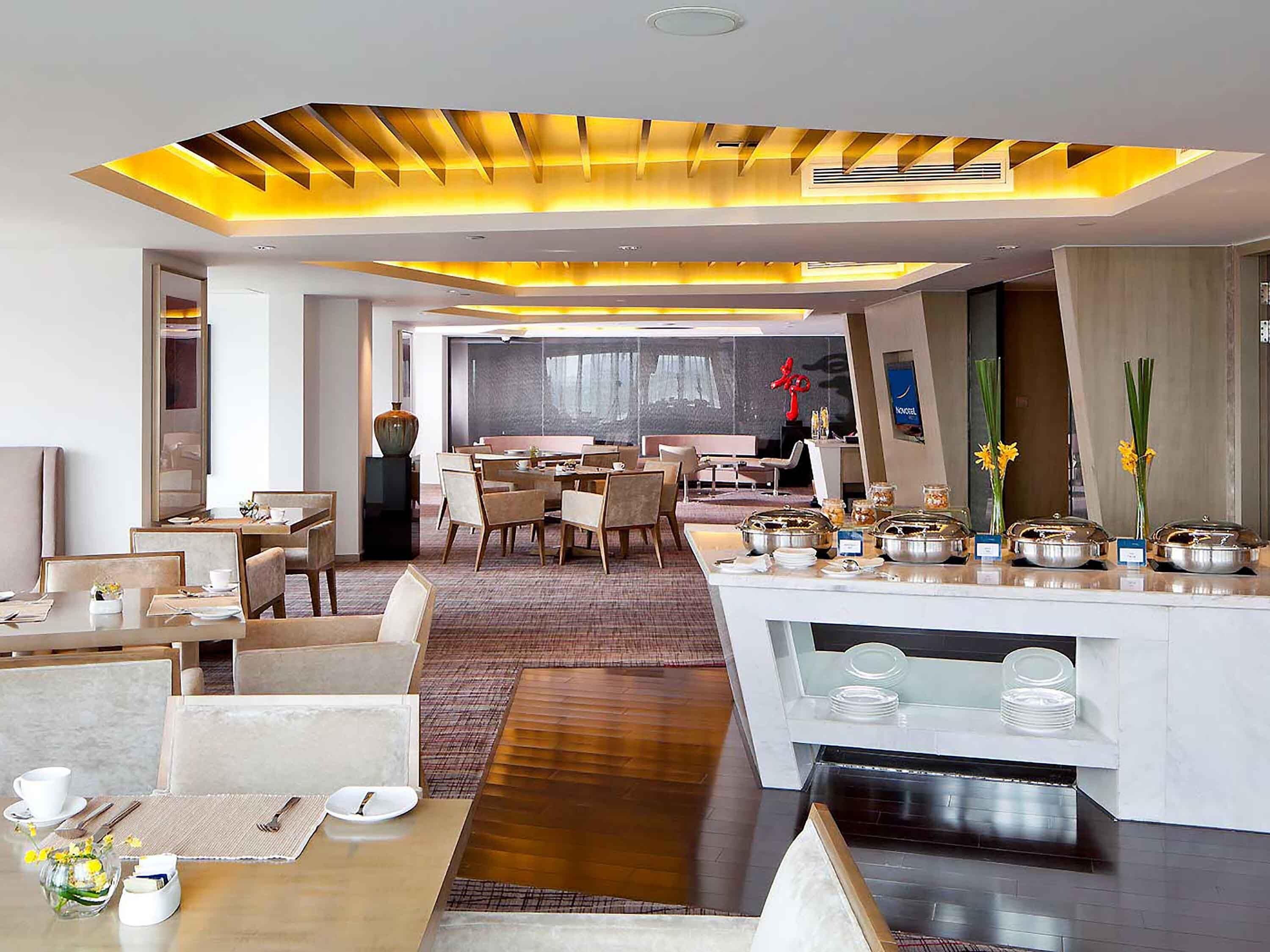 A modern hotel lobby with a dining area, a reception desk, and a view of the city.