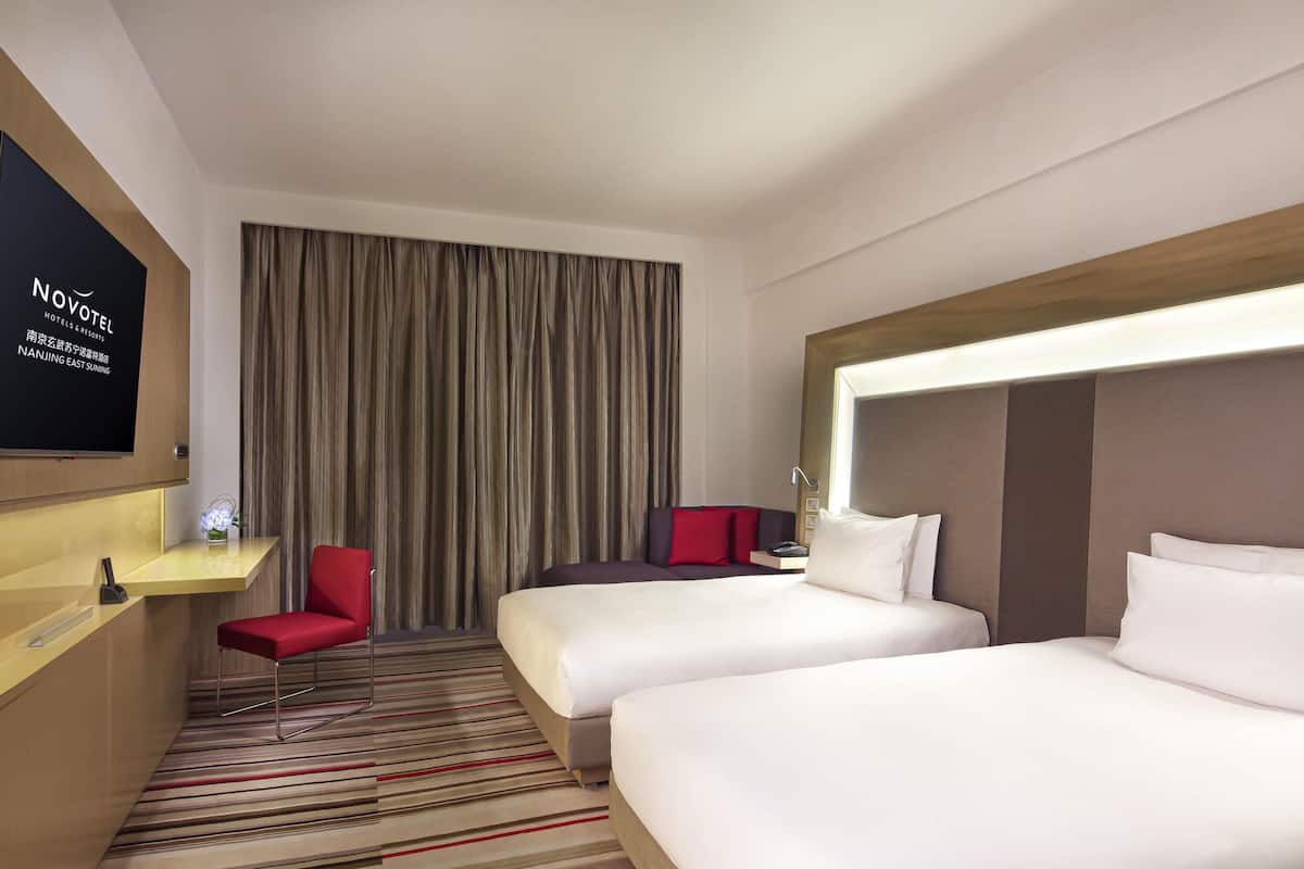 Une chambre d’hôtel équipée d’un lit, d’un bureau, d’une chaise, d’une télévision et d’une grande fenêtre avec des rideaux.