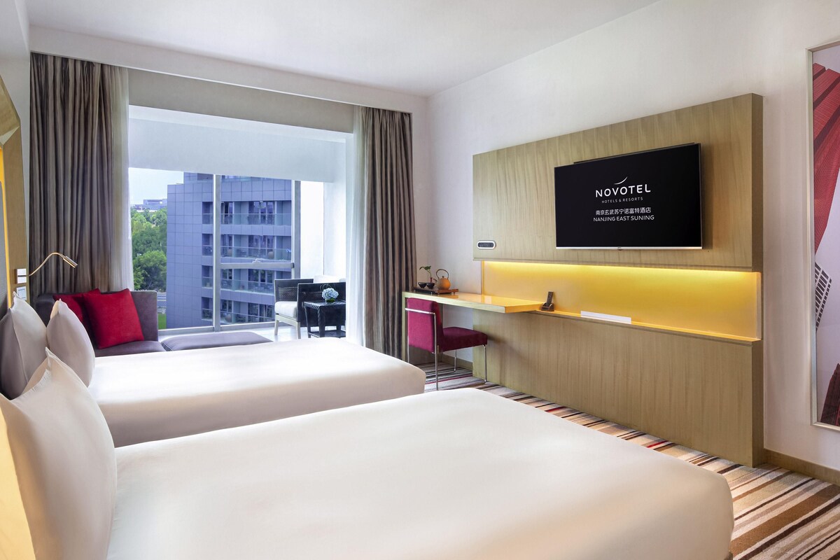 Une chambre d’hôtel avec deux lits, un bureau, une télévision et une vue sur un immeuble.