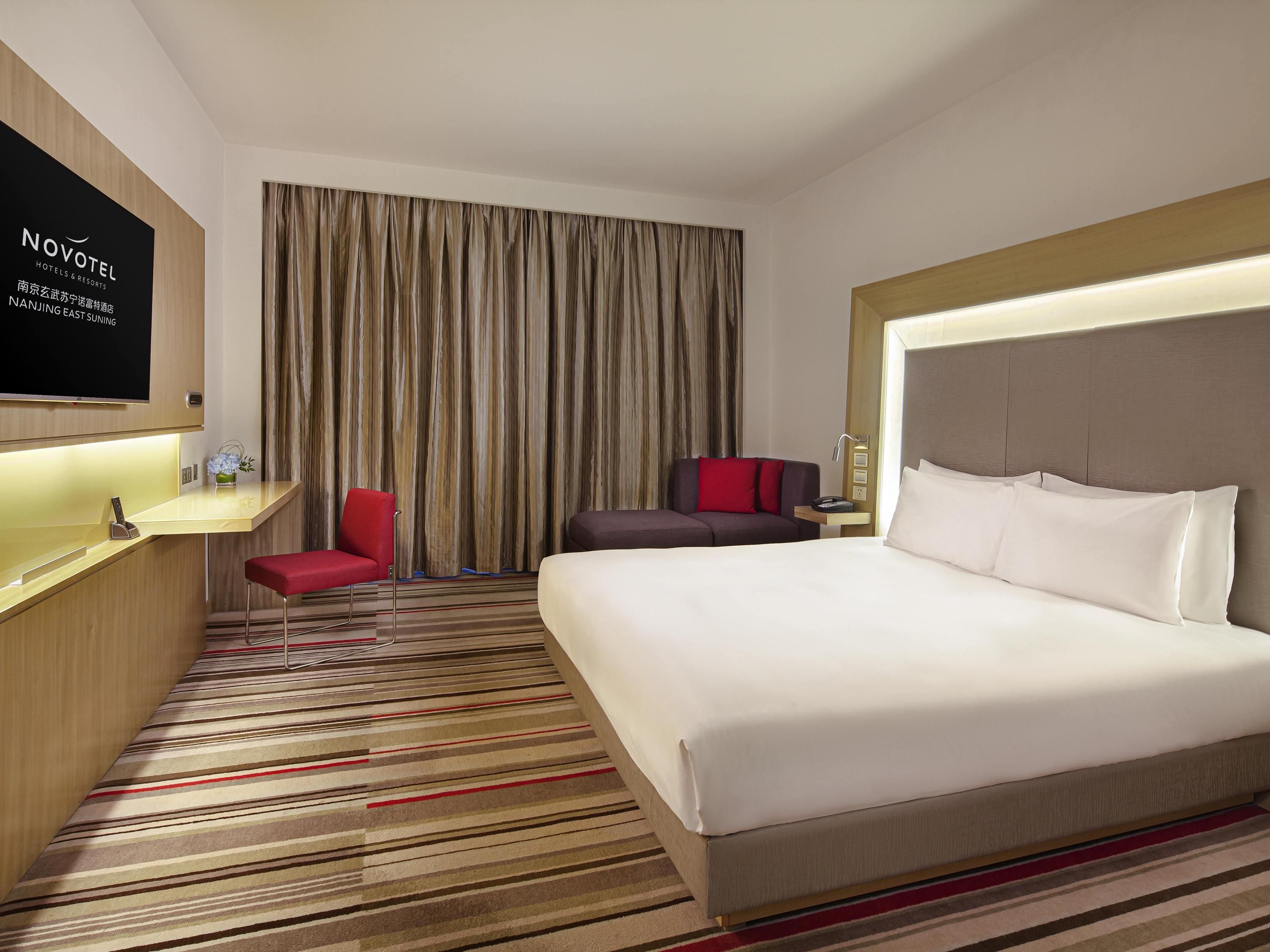 A hotel room with a large bed, a desk, a chair, a TV, and a curtain.