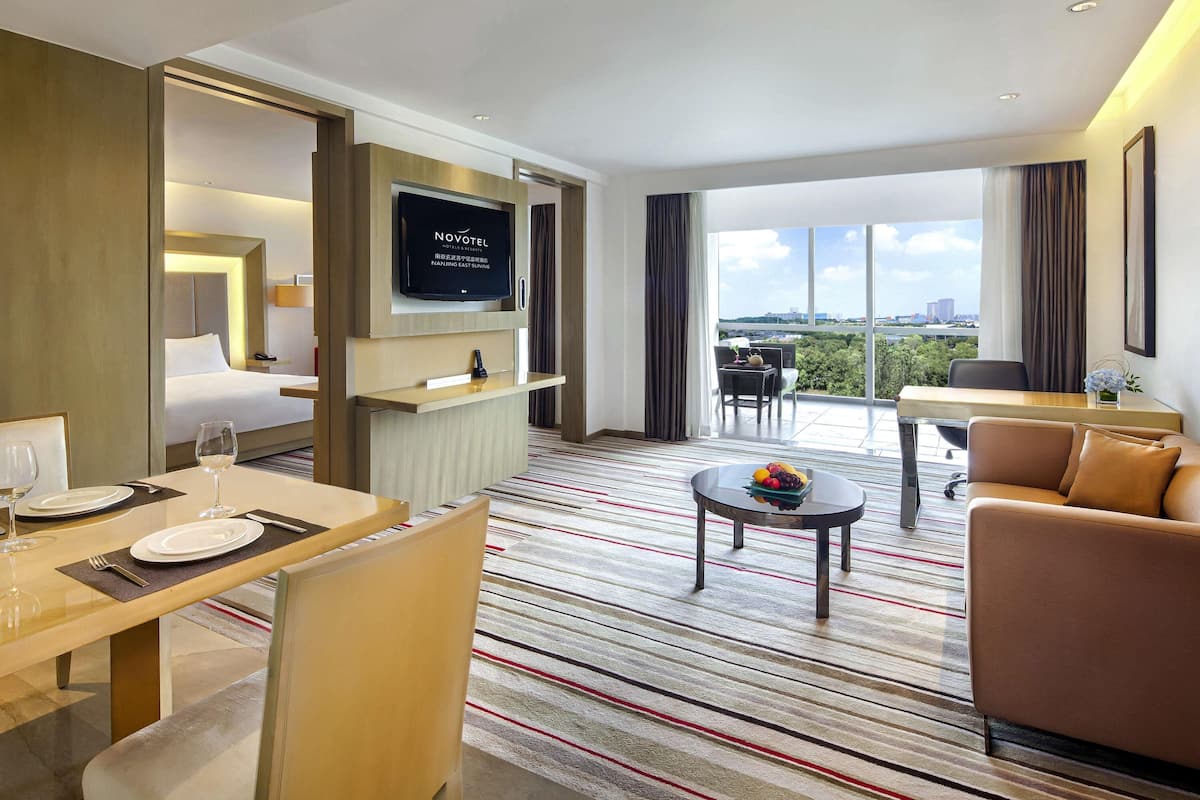 Une chambre d’hôtel comprenant un lit, une télévision, un coin repas avec une table et des chaises, un canapé et un balcon avec vue.