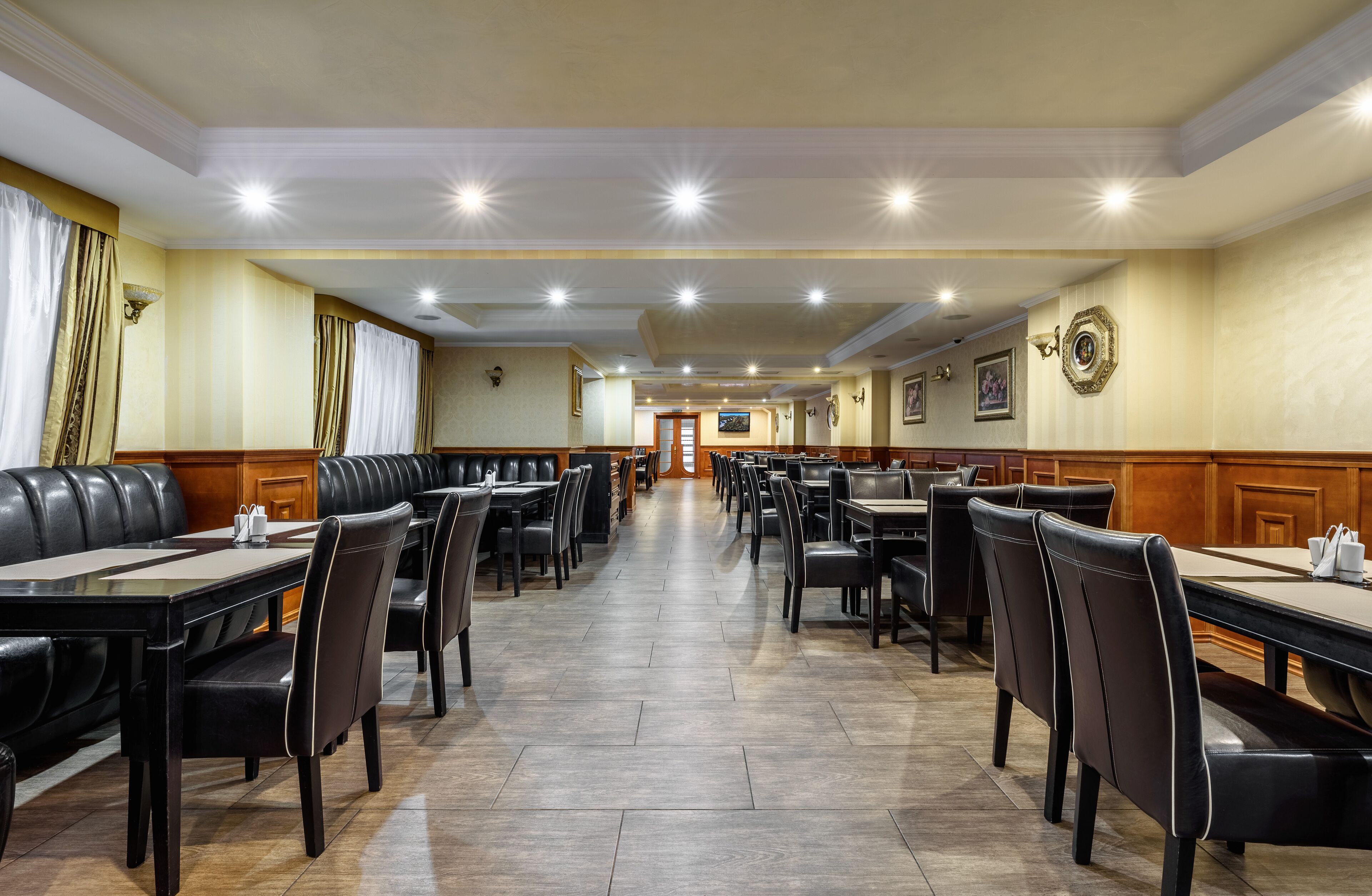 Ein geräumiges Restaurant mit mehreren Tischen und Sitzgelegenheiten, Holzböden und eingelassener Deckenbeleuchtung.