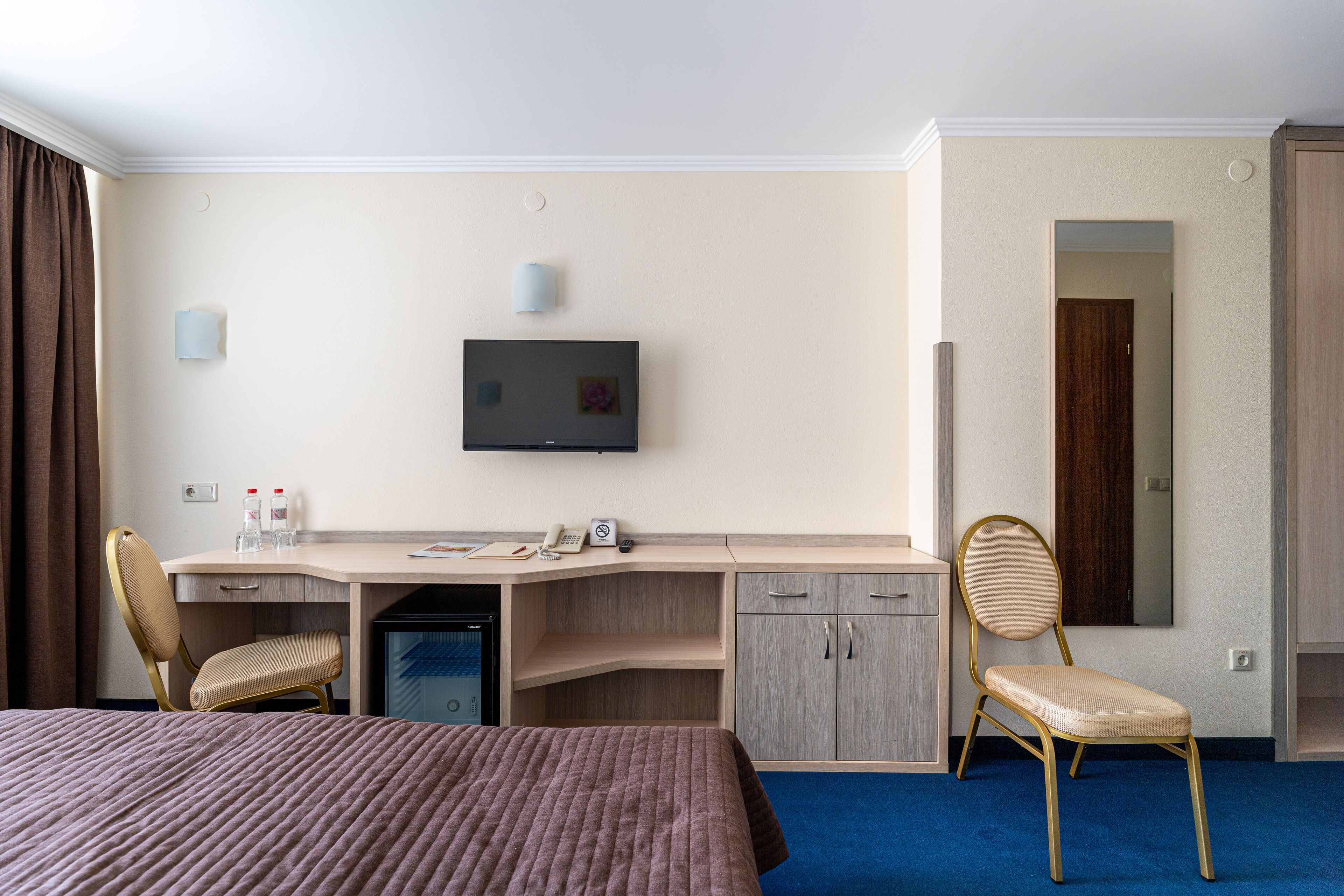 Habitación de hotel con cama, escritorio, silla, televisor y un refrigerador pequeño.