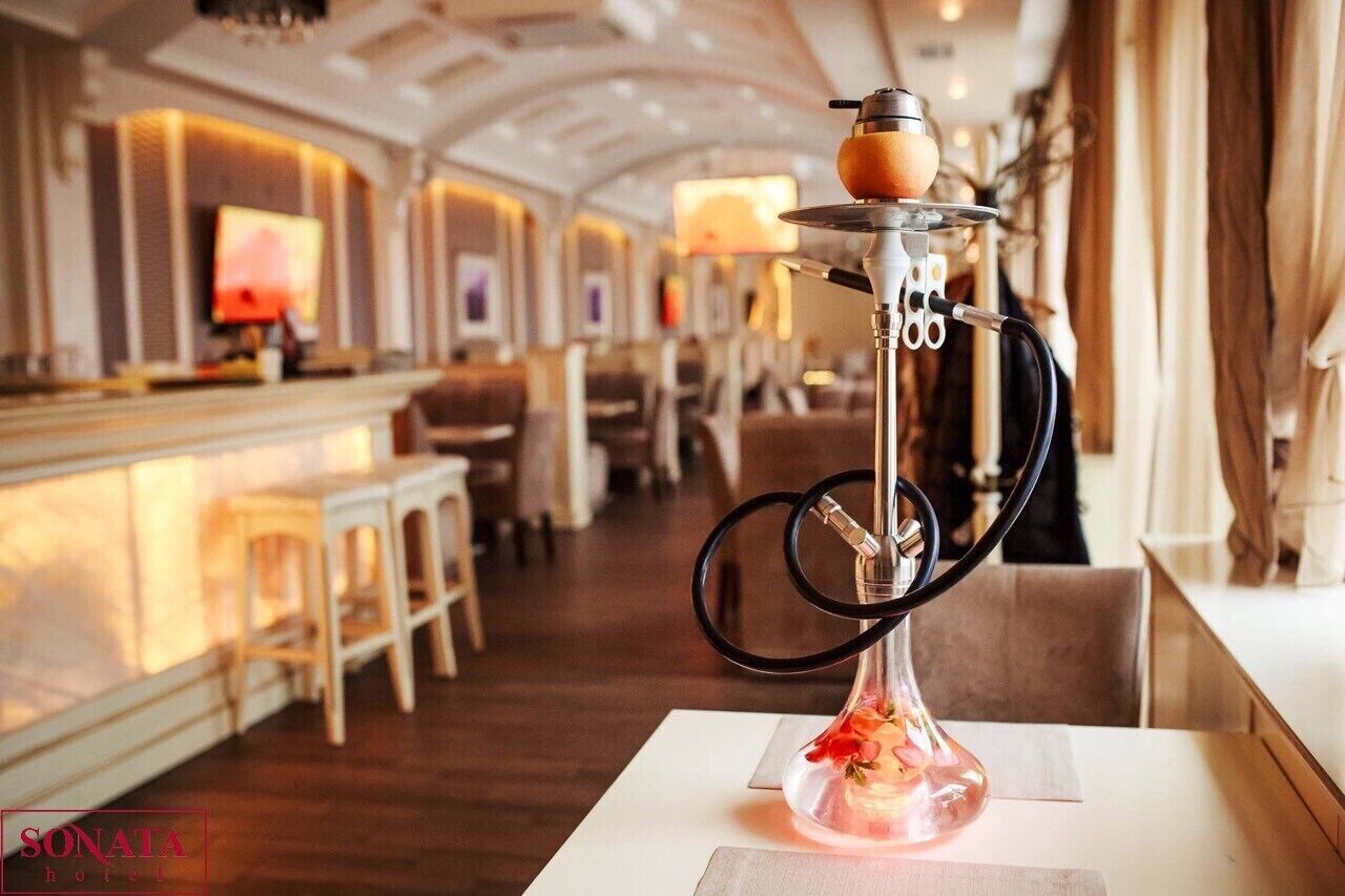 Een shisha op een tafel in een hotellobby, met een bar en zithoek op de achtergrond.