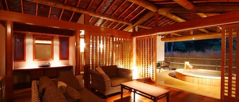 A cozy interior with a wooden ceiling, a seating area with sofas and a table, and a hot tub area visible through a partition.