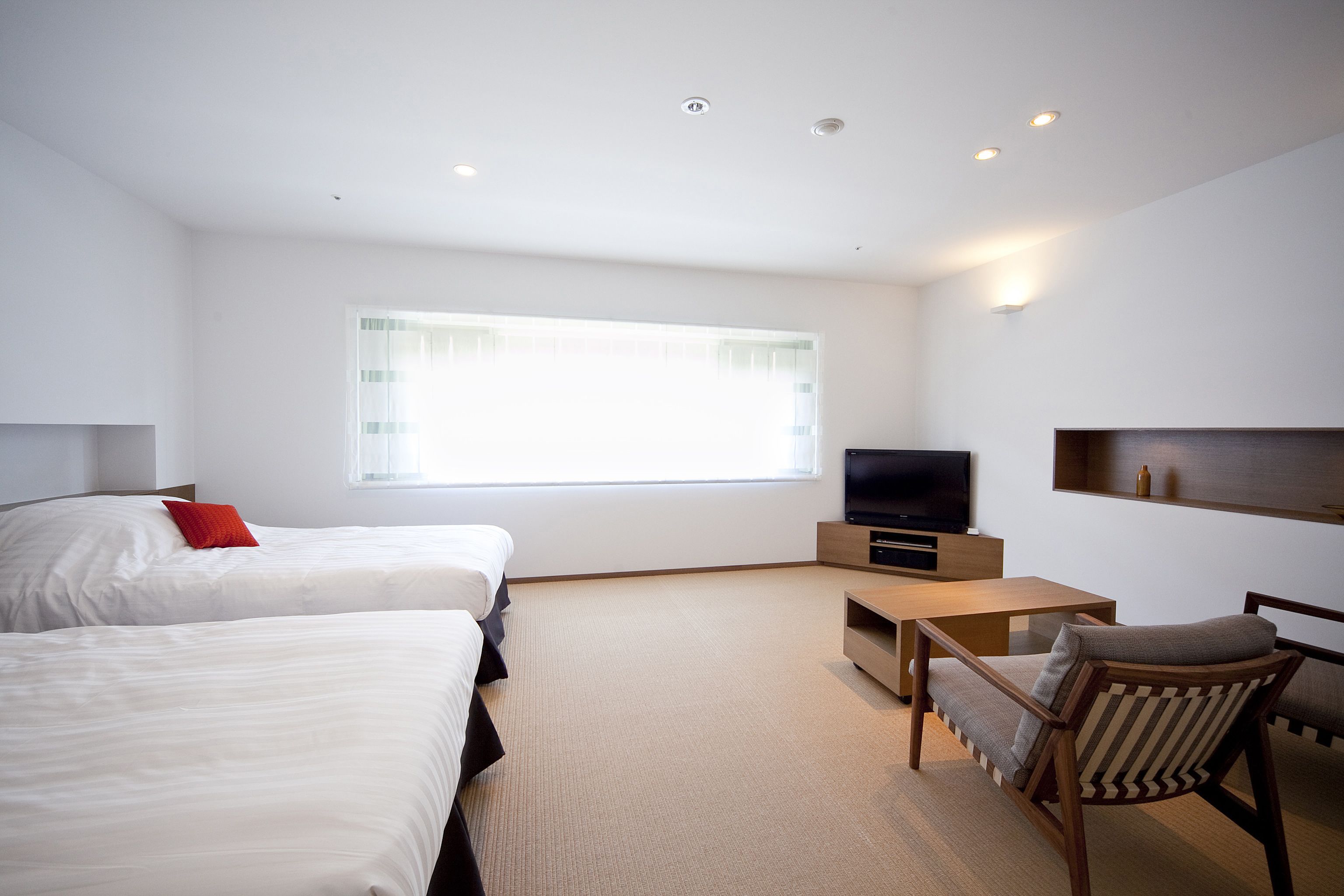 A hotel room with two beds, a TV, a wooden coffee table, and a chair.