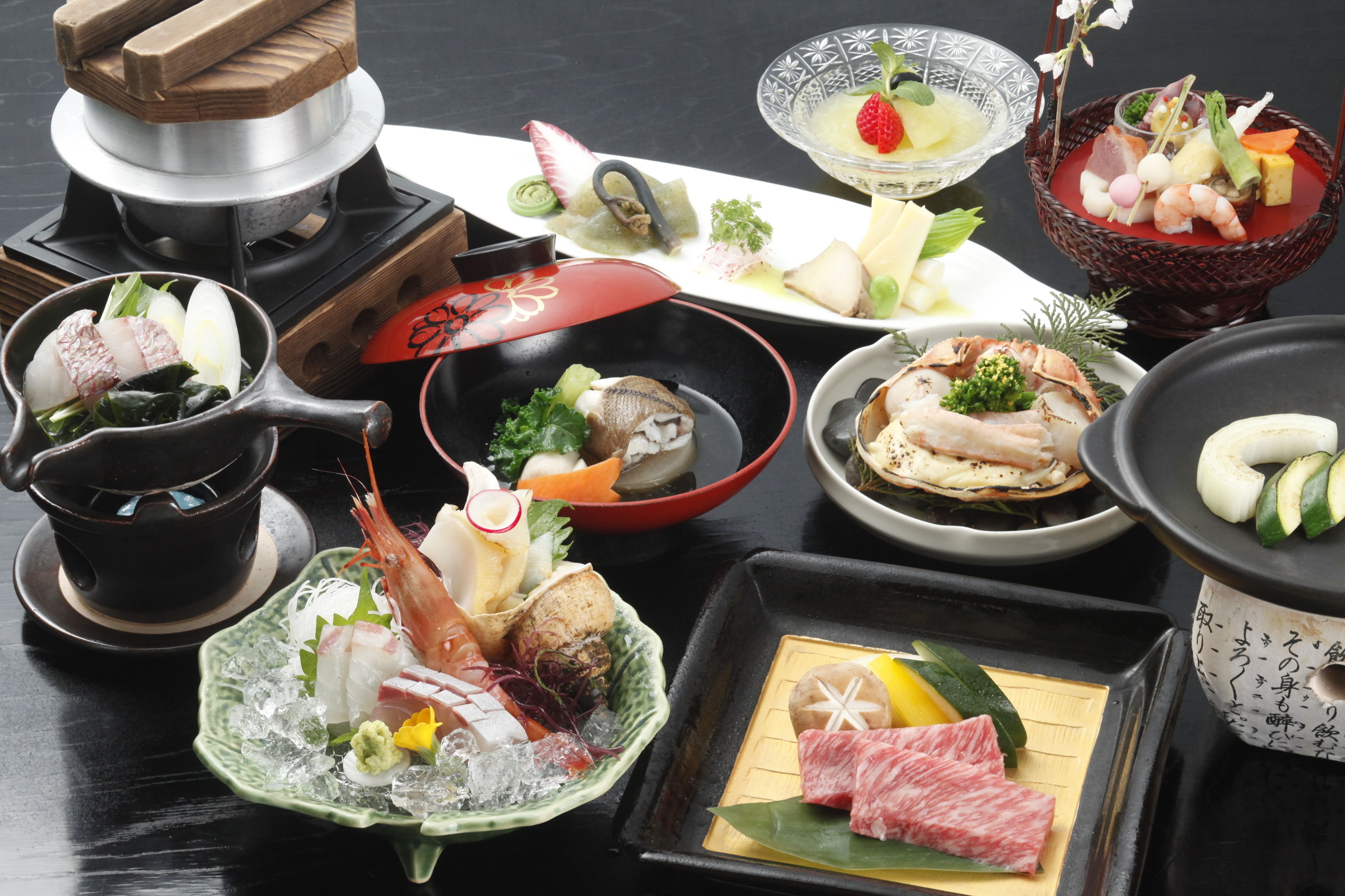 A variety of dishes including seafood, vegetables, and meat, arranged on a table with a teapot and a traditional Japanese tea set.