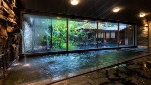 Een wellnessruimte met een warmwaterbron, stenen muren en uitzicht op een bos door grote glasramen.