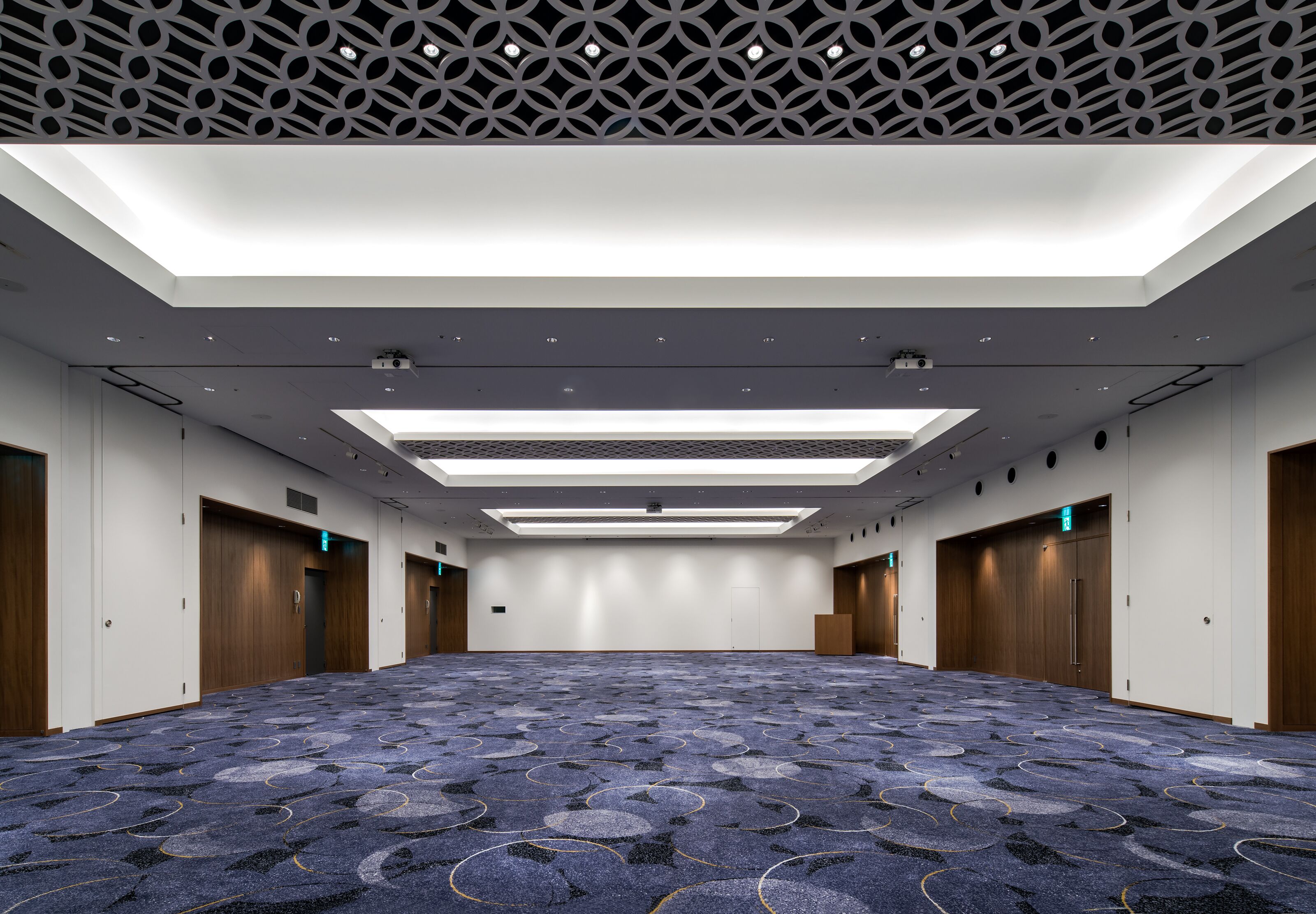 A large, well-lit conference room with a patterned carpet, wooden doors, and a modern ceiling design.