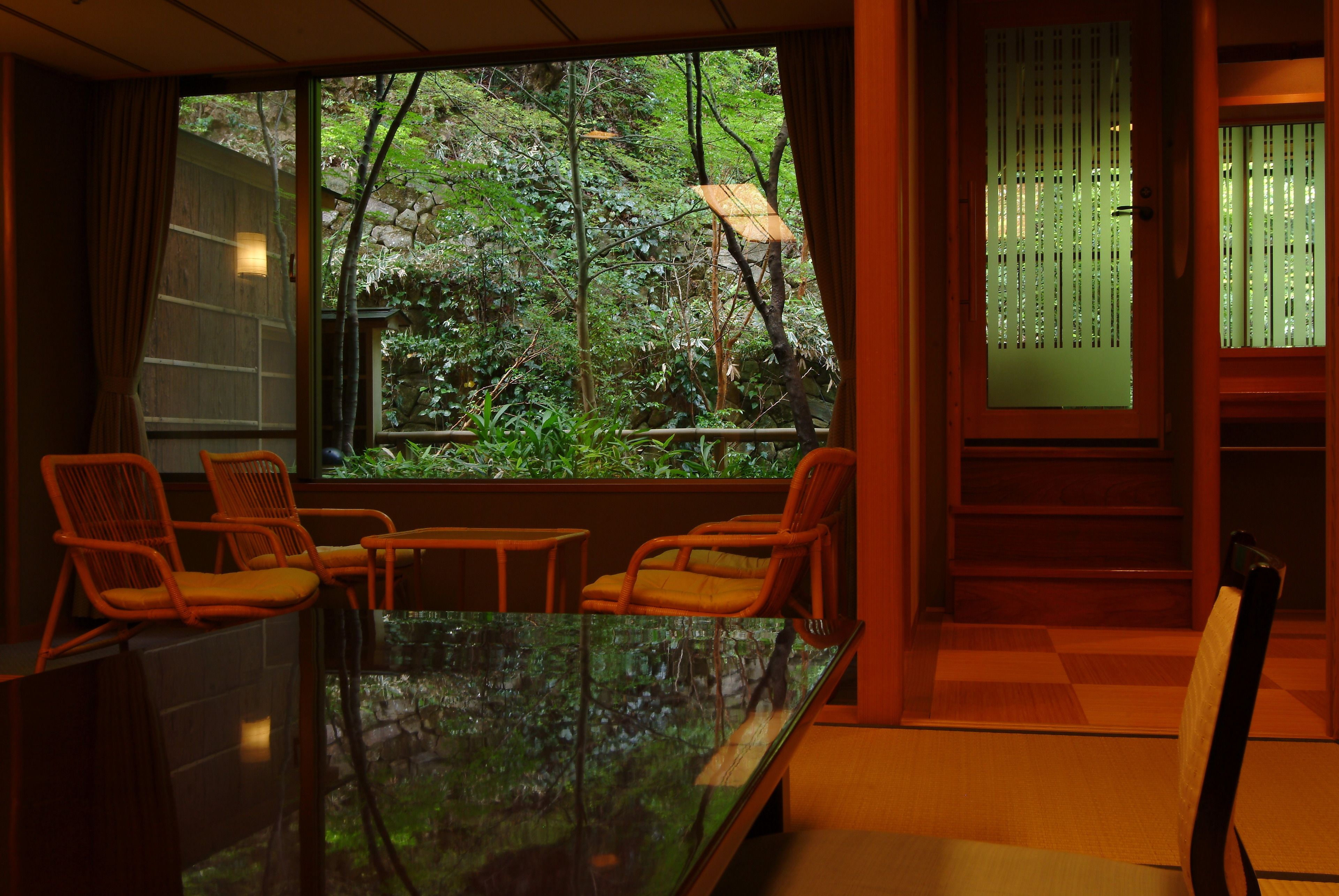 A room with a large window, a glass table, and orange chairs.
