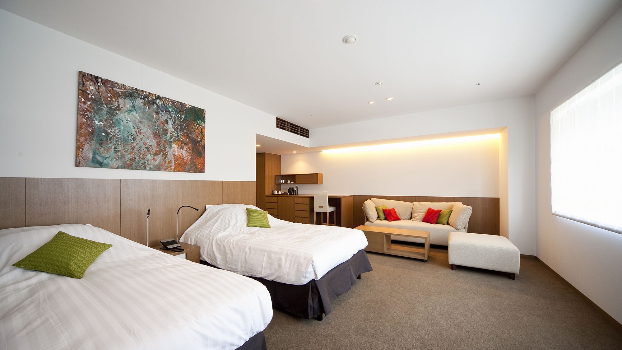 Une chambre d’hôtel avec deux lits, un bureau, une chaise, une petite kitchenette et une grande fenêtre.