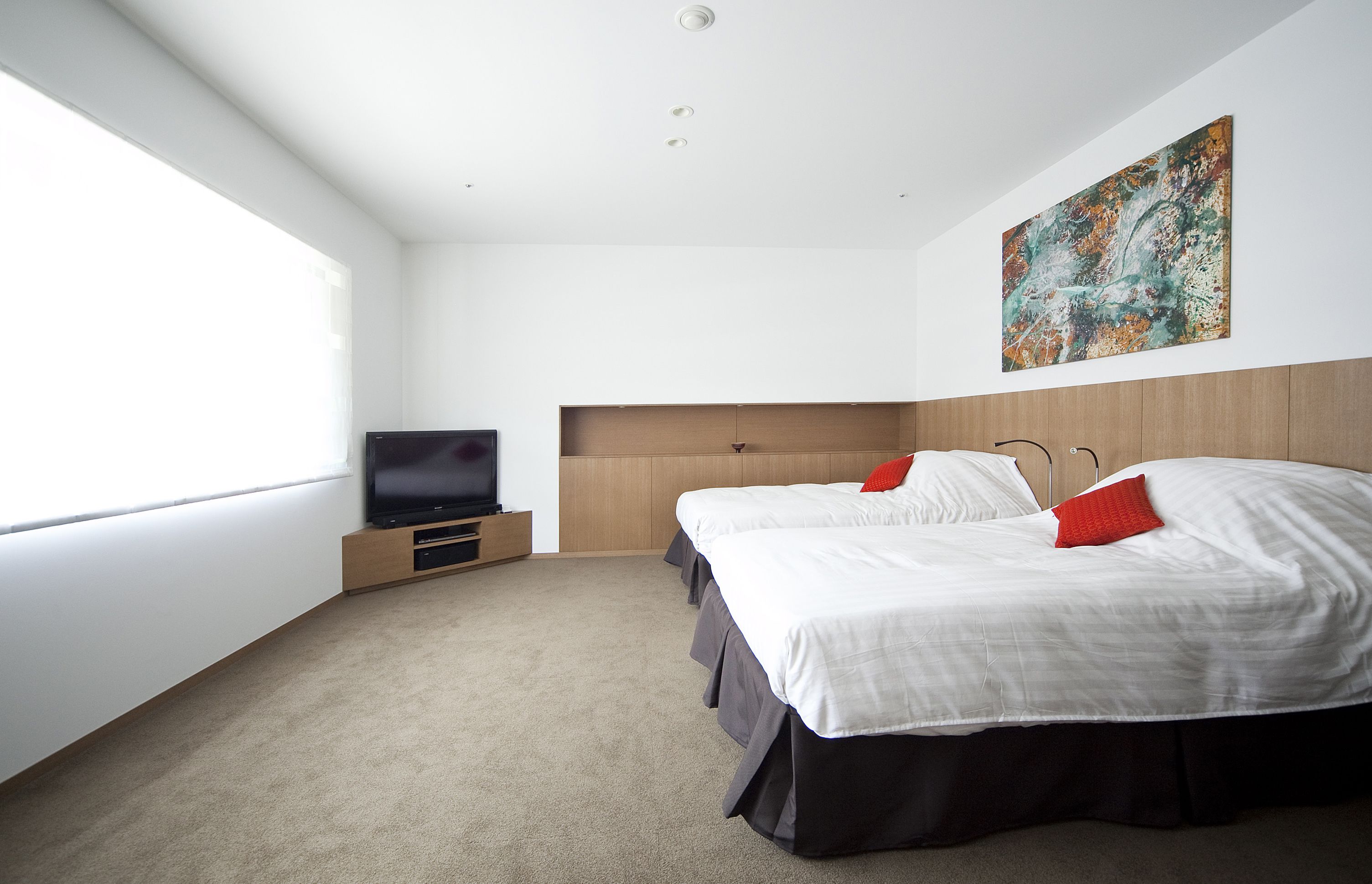A hotel room with two beds, a TV, a wooden headboard, and a large window.