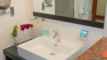 A bathroom with a white sink, a mirror, and toiletries on a shelf.