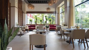 A spacious indoor dining area with multiple tables and chairs, large windows with a view of greenery, and decorative wicker lighting fixtures. - Royal Torarica Hotel (Paramaribo)