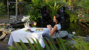 A woman dining at an outdoor table with a view of a waterfall and lush greenery. - Royal Torarica Hotel (Paramaribo)