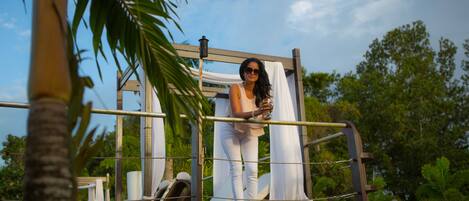 A person standing on a balcony with a view of palm trees and a clear sky.