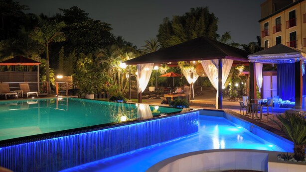 A swimming pool with a waterfall feature, surrounded by outdoor seating and covered areas. - Royal Torarica Hotel (Paramaribo)