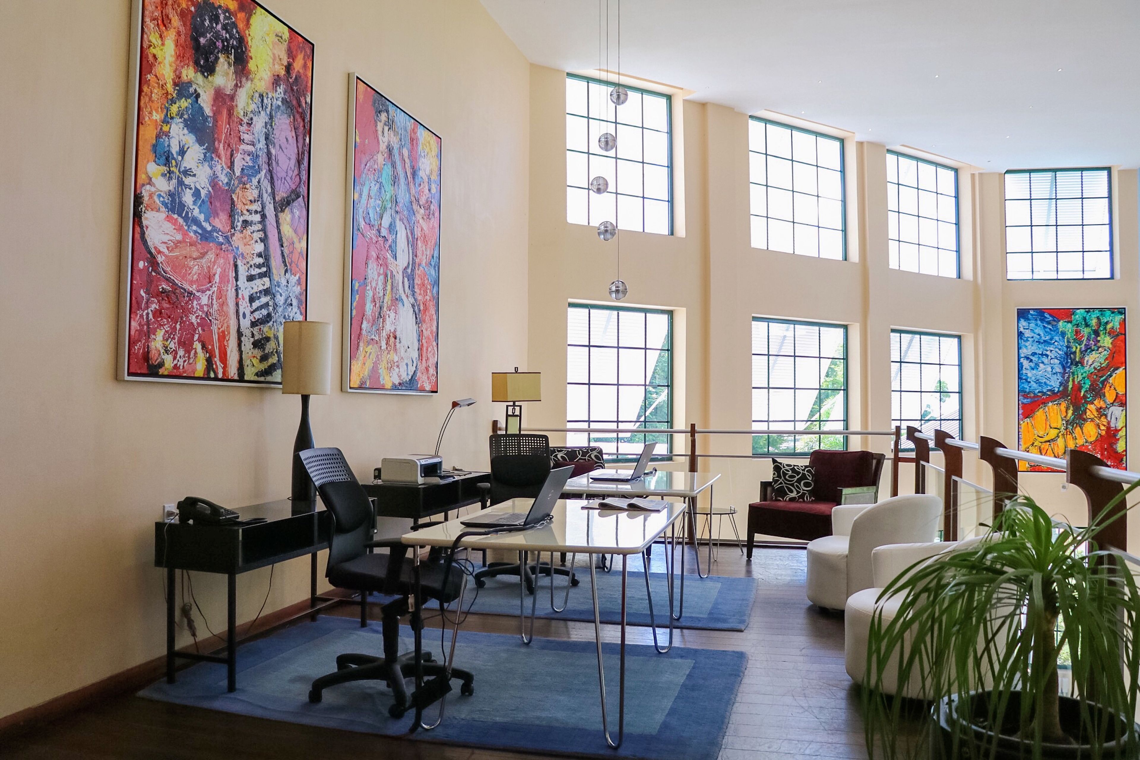 Una oficina amplia con ventanas grandes, muebles modernos y obras de arte coloridas.