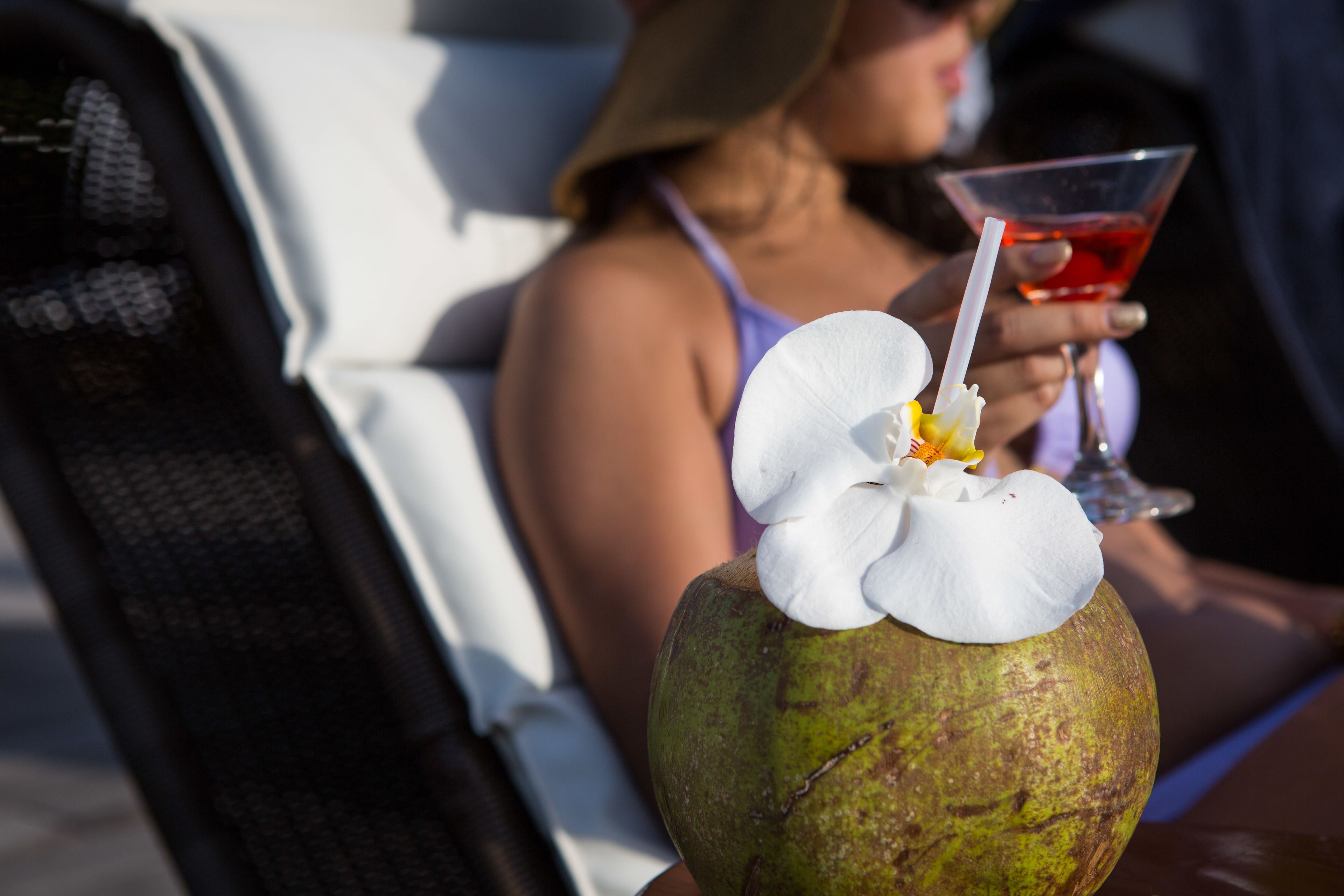 Una persona sosteniendo una bebida con pajita y un coco decorado con una orquídea.