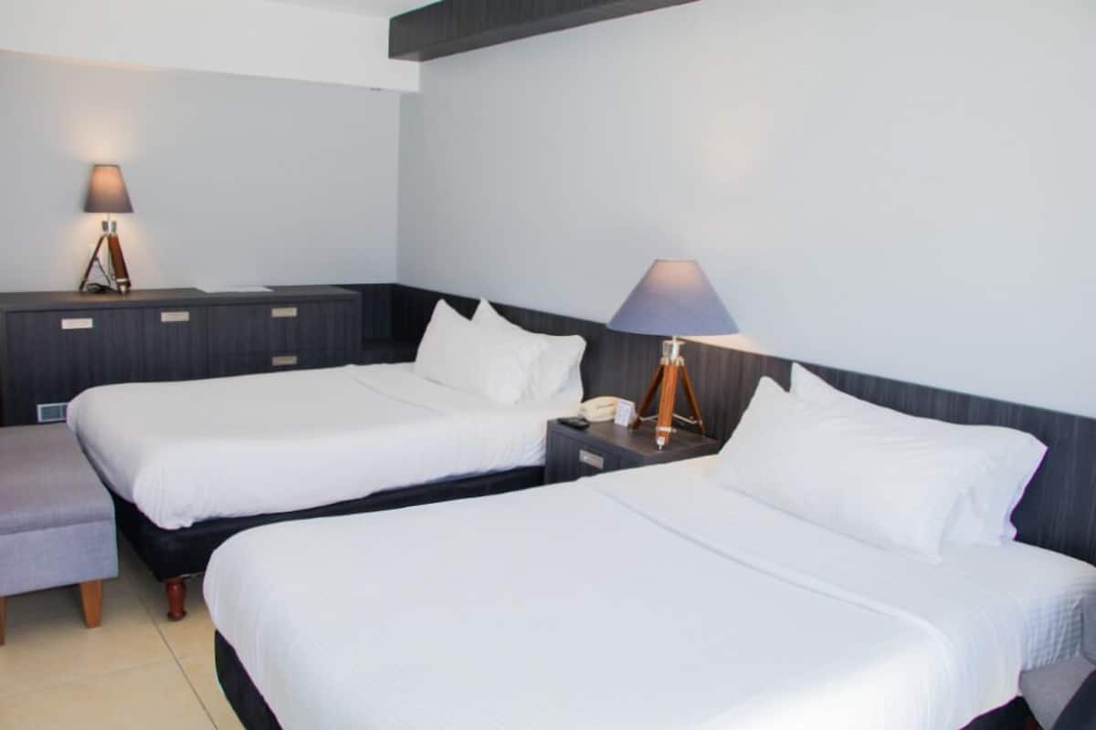 A hotel room with two single beds, a bedside table with a lamp, and a small seating area.