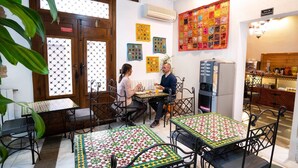 Un café acogedor con mobiliario de madera, manteles estampados y un colorido colcha en la pared.