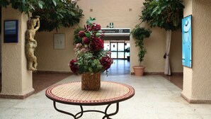 Un pasillo con una mesa redonda en el centro, rodeada de plantas en macetas y una estatua.