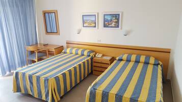 Une chambre d’hôtel avec deux lits simples, un bureau, une chaise et deux tableaux encadrés au mur.