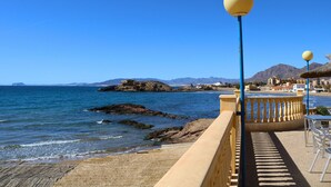Un paseo marítimo con barandilla, vistas despejadas al mar y montañas a lo lejos.