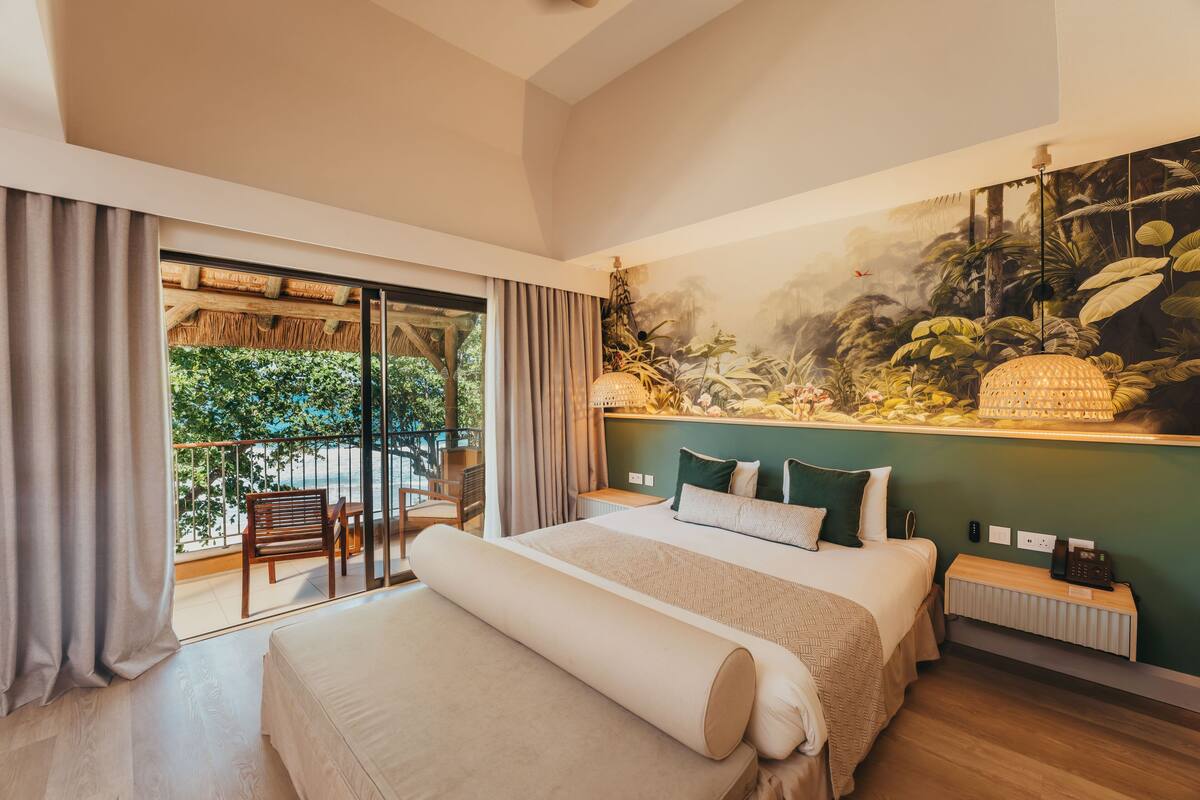 Een ruime slaapkamer met een groot bed, een balkon met uitzicht op groen, en een mural met een tropisch thema op de muur.