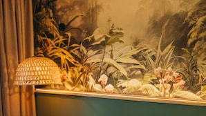 Quarto de hotel com cama, almofadas, um mural na parede, luminária e cortinas.