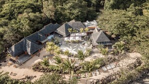 Vista aérea de um resort com vários edifícios, um pátio central e palmeiras ao redor.