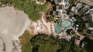 Vista aérea de um resort com várias piscinas, uma praia e vegetação exuberante.