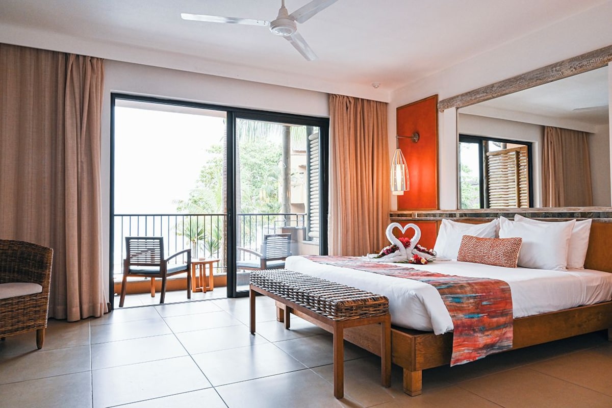 Ein geräumiges Schlafzimmer mit einem großen Bett, einem Balkon mit Sitzgelegenheiten und Blick auf Grünflächen.