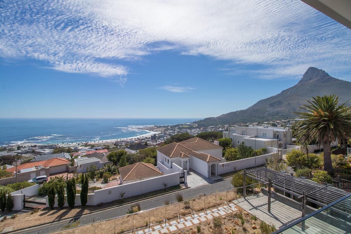 A coastal residential area with white buildings, a palm tree, and a view of the ocean and a mountain in the distance.