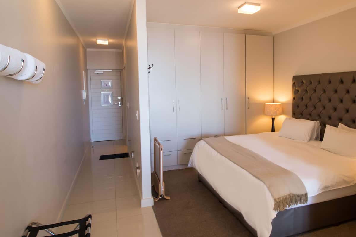 A hotel room with a large bed, a wardrobe, a bedside table with a lamp, and a flat-screen TV.