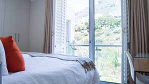 Ein Hotelzimmer mit Bett, einem Fenster mit Vorhängen, einem Balkon und Blick auf eine gebirgige Landschaft.